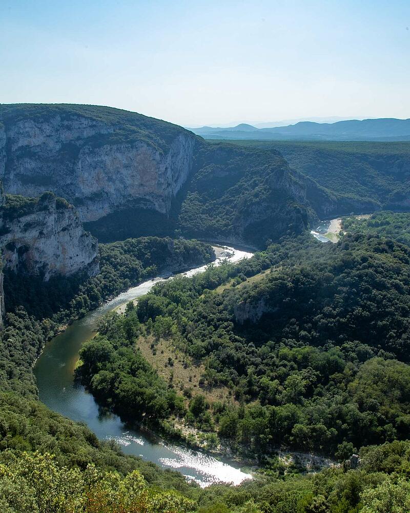 [Translate to Espagnol:] Panoramic high angle view of the green Ardeche river canyon winding through deep forests and massive stone cliffs near Les Castels campsites.
