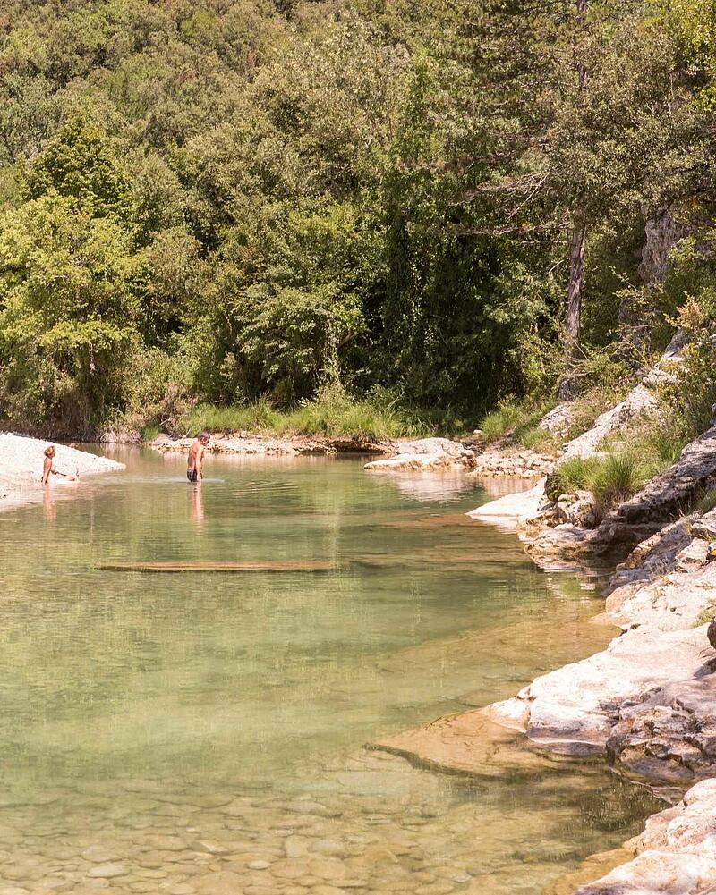 [Translate to Espagnol:] People relaxing and swimming in the clear waters of a wild river near Les Castels luxury campsites in Ardèche, France.