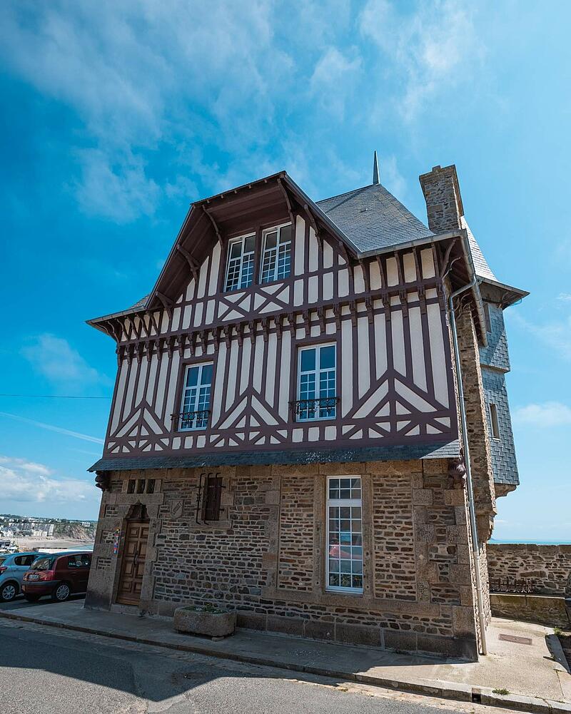 [Translate to Espagnol:] A beautiful historic building combining a stone ground floor with upper levels featuring traditional half-timbered architecture, discovered while staying at Les Castels.