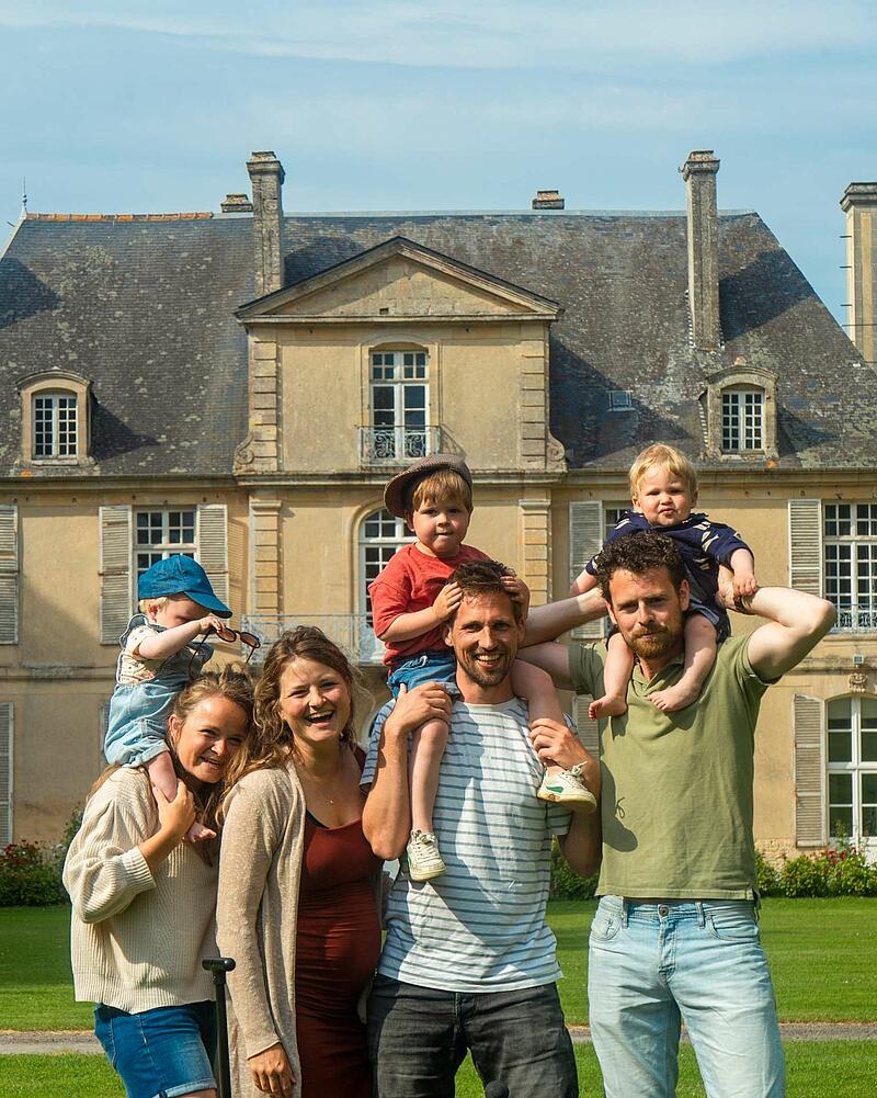 [Translate to Espagnol:] A joyful group photo of adults and young children smiling together in front of a historic French chateau at a luxury Les Castels holiday estate.